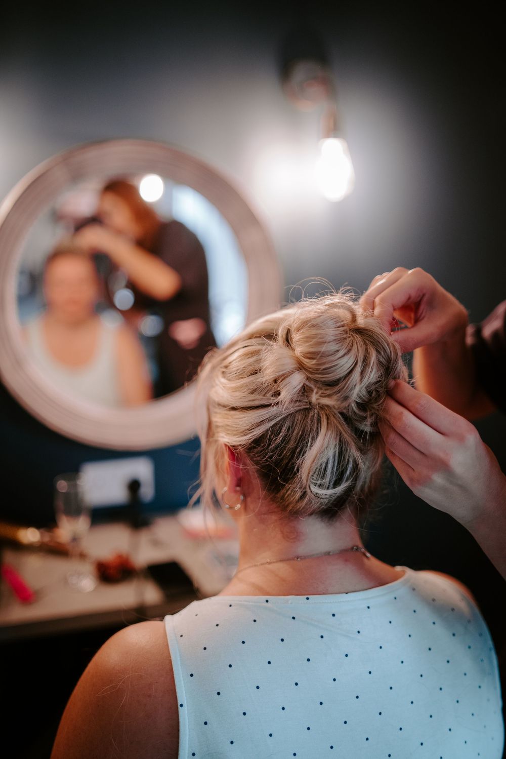 Close-up of hairstylist pinning elegant updo bun on blonde bride before wedding ceremony.
