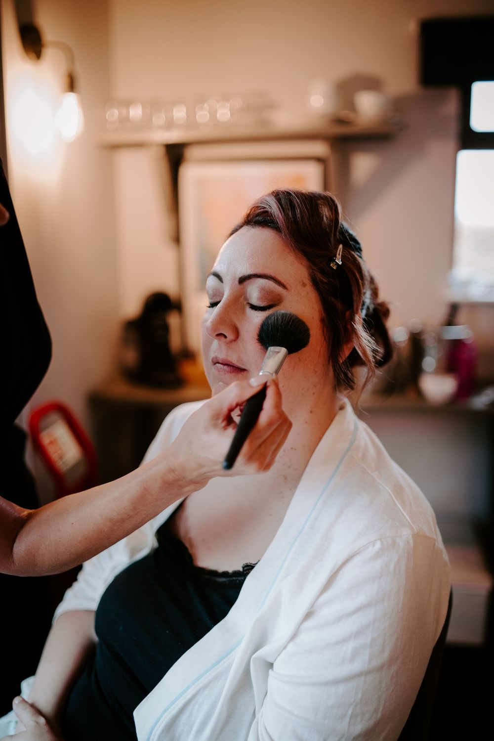 Bride gets makeup applied with a powder brush during wedding day preparations.