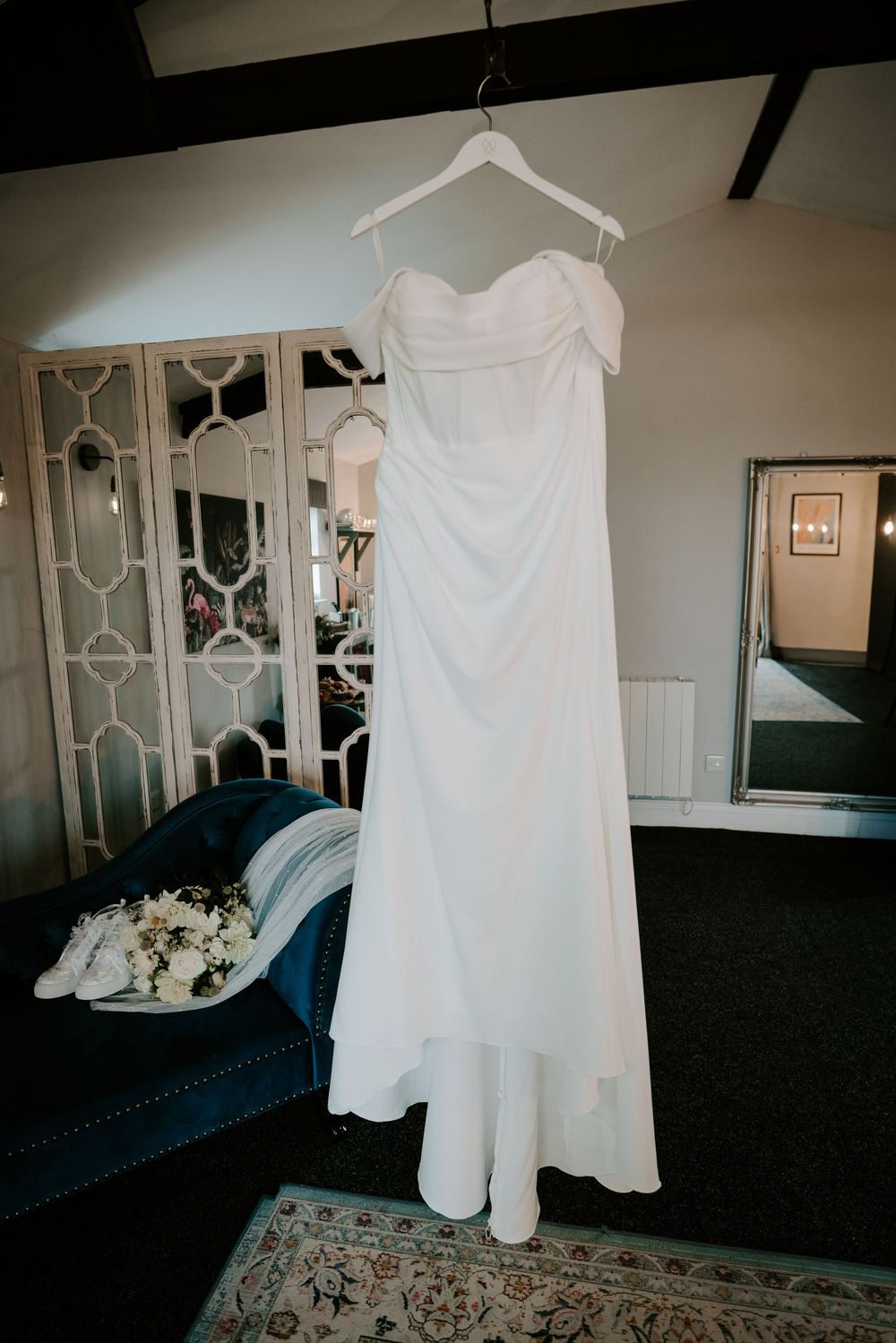 Elegant off-shoulder white wedding dress hanging on a hanger in a beautifully decorated bridal suite.