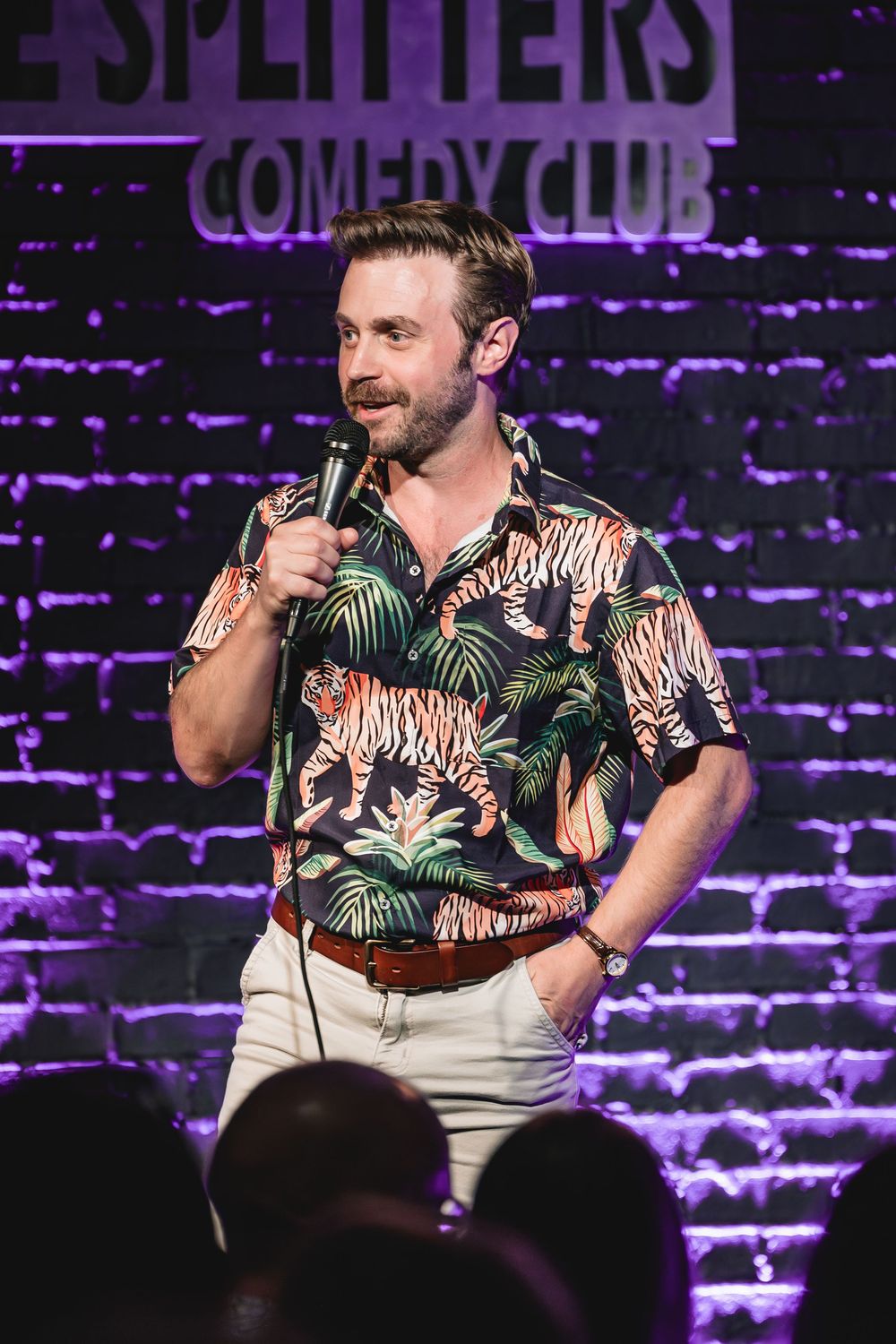 Tyler Fischer the Comedian performs stand-up at Splitters Comedy Club wearing a tropical tiger-print shirt, holding a microphone on stage.