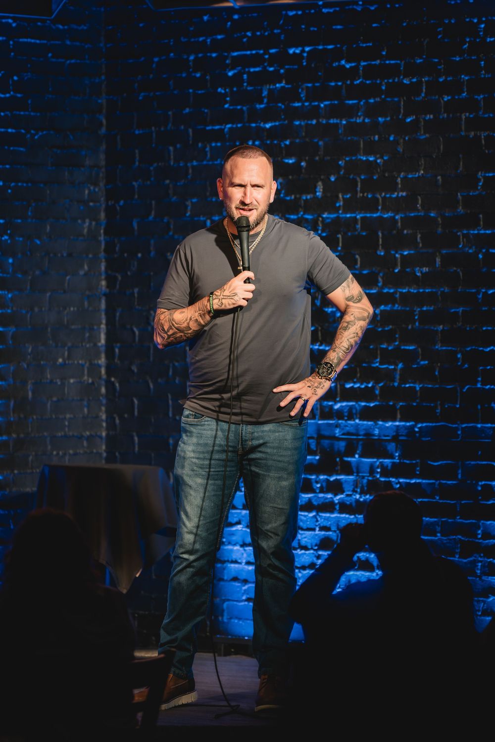Kevin Eudy the comedian at Side Splitters. Male stand-up comedian performing on stage with microphone in front of blue-lit brick wall.