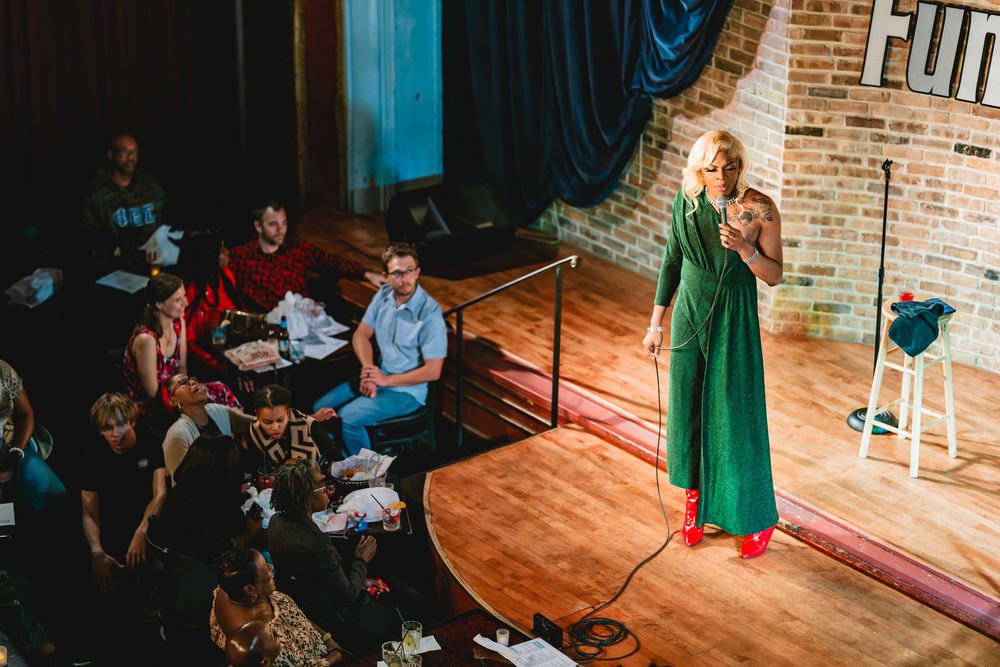 Ms Renee the comedian. Blonde black comedian in green jumper dress performing on stage at Funny Bone comedy club.