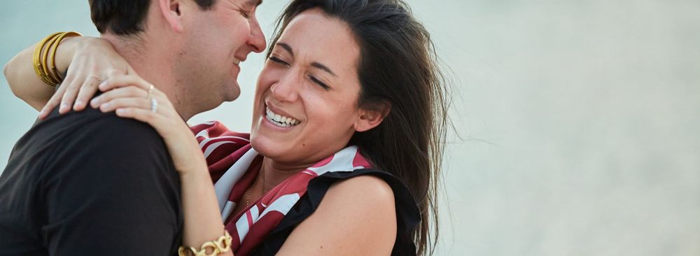 Happy woman laughing and hugging man during romantic beach engagement celebration.