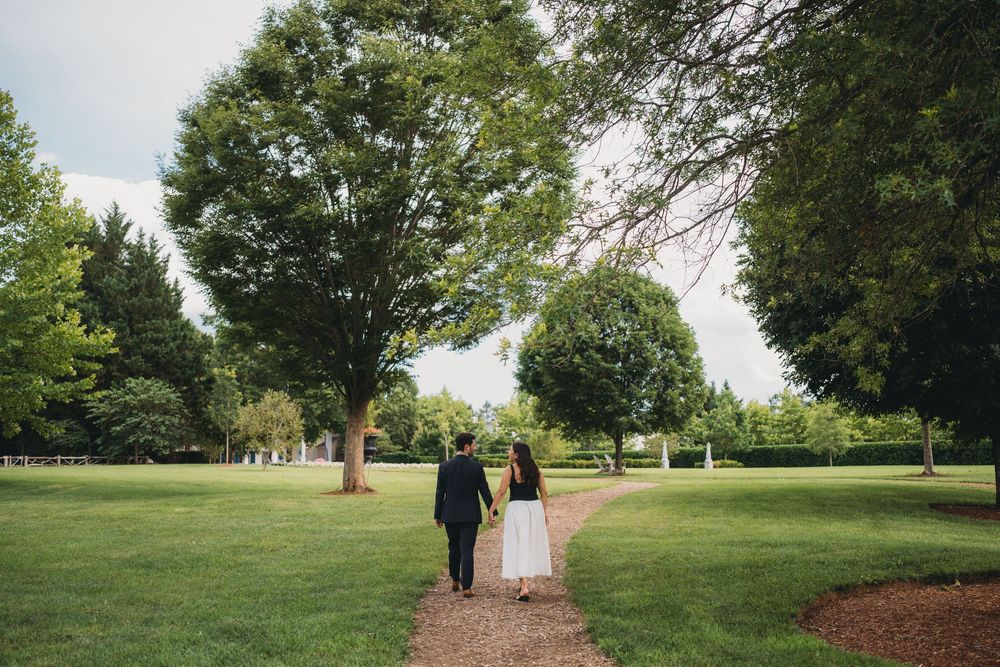 A couple walks hand-in-hand along a garden path surrounded by lush green trees on their wedding day.