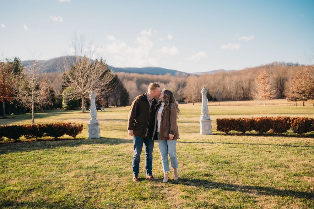 Couple embracing in a scenic garden with mountain views and manicured hedges on a sunny autumn day.