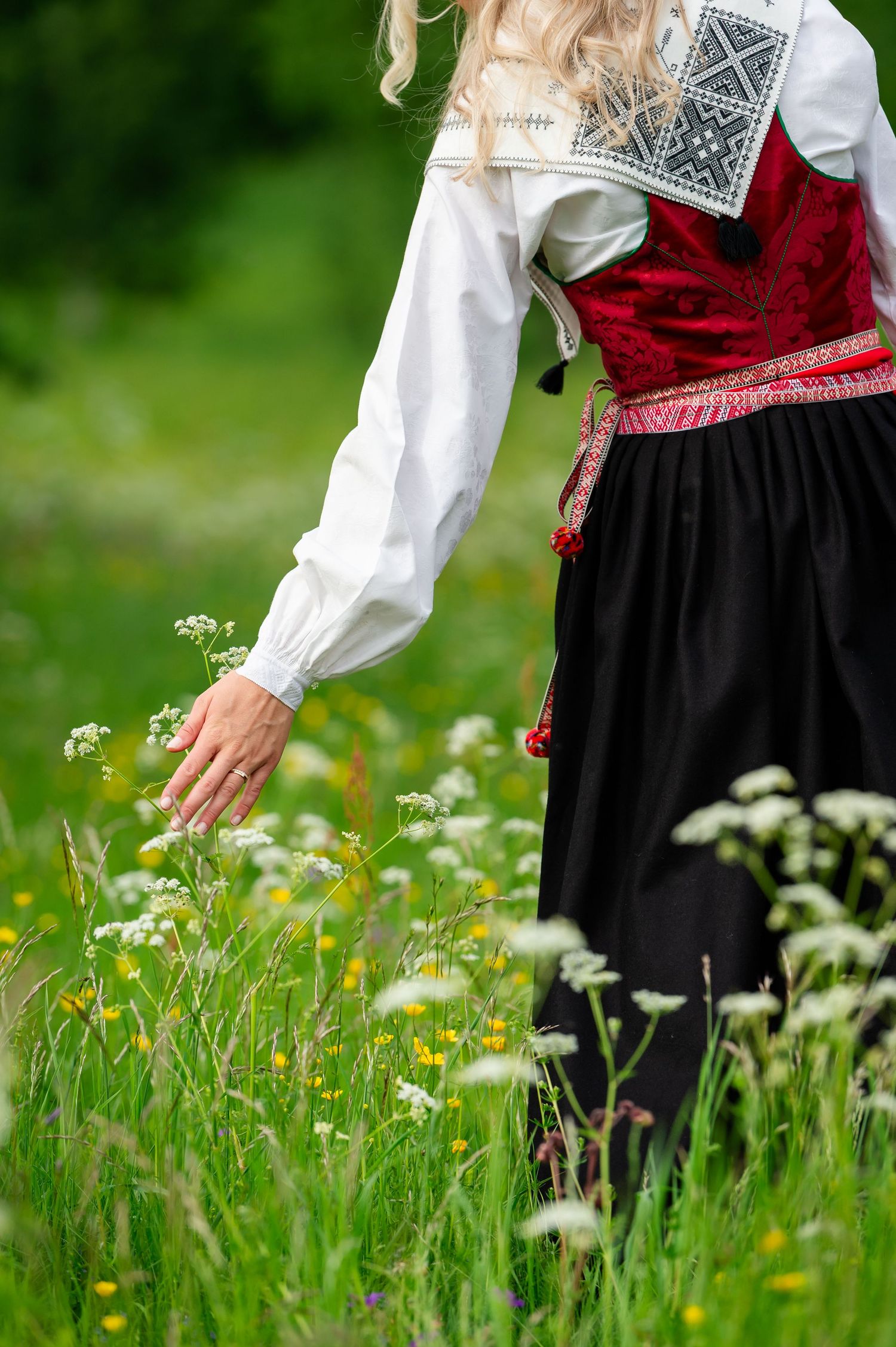 Woman in traditional folk costume touching wildflowers in a green meadow.