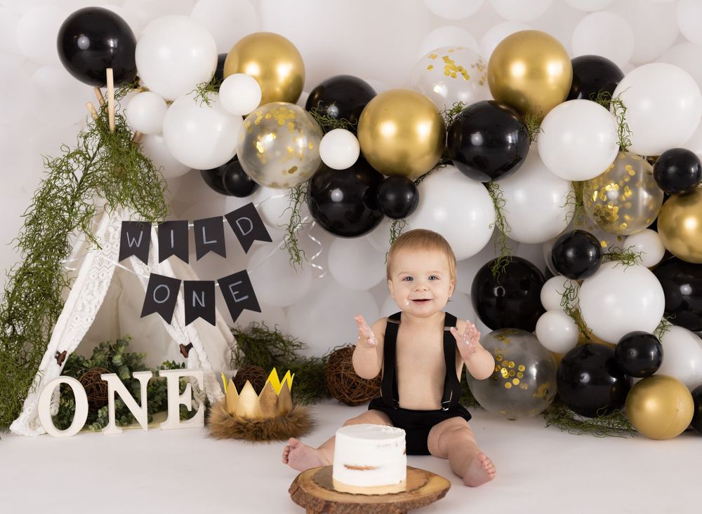 Baby's first birthday cake smash with black, white, and gold balloon garland and Wild One teepee backdrop.