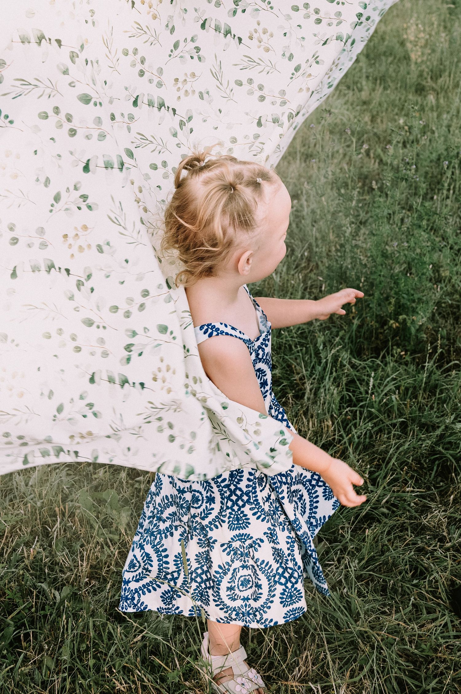 Kleines Mädchen im Sommerkleid spielt mit einem geblümten Tuch auf einer Wiese.