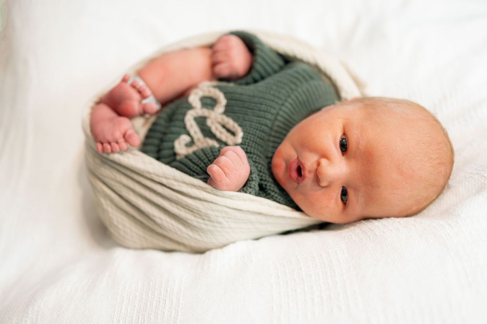 Newborn baby wrapped in cream knit blanket wearing green outfit during a Fresh 48 session at Parkwest Medical Center in Knoxville, TN.