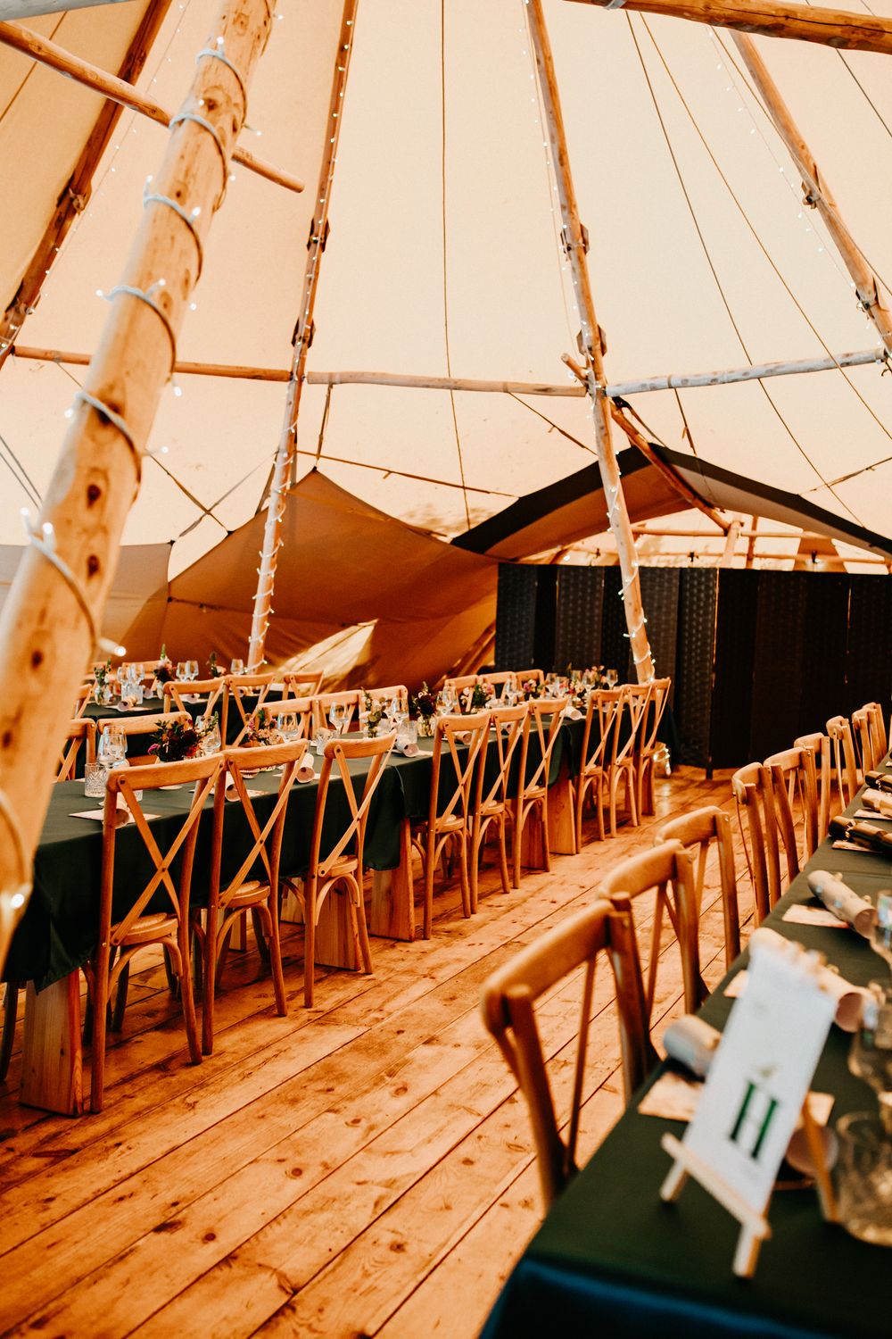 Interior of a rustic whatton tipi wedding venue with long dining tables, cross-back chairs, and warm ambient lighting on timber flooring.