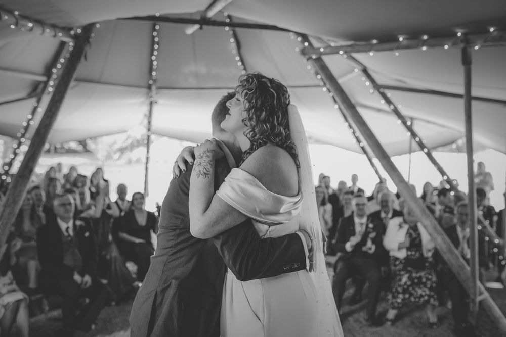 Black and white photo of a couple after completing their vows under a fairy light tent at a wedding reception.