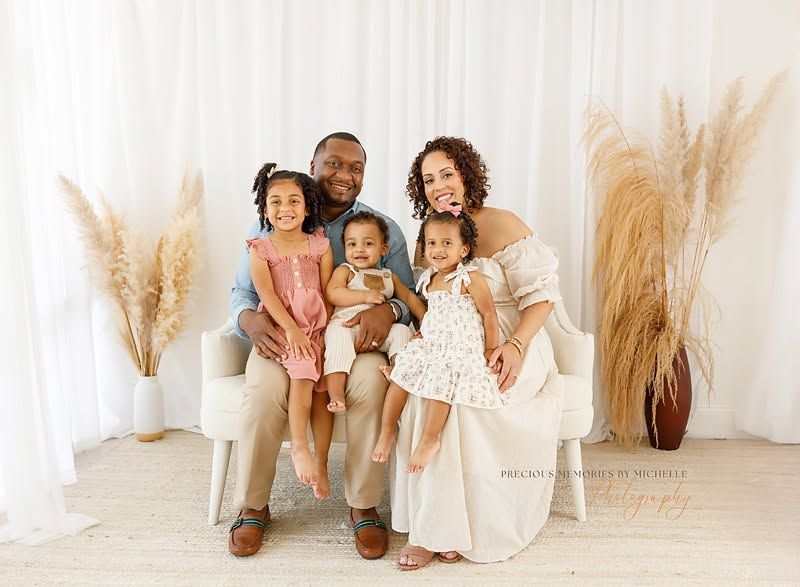 A joyful family of five poses together in a bright white studio with pampas grass decor for a professional portrait.