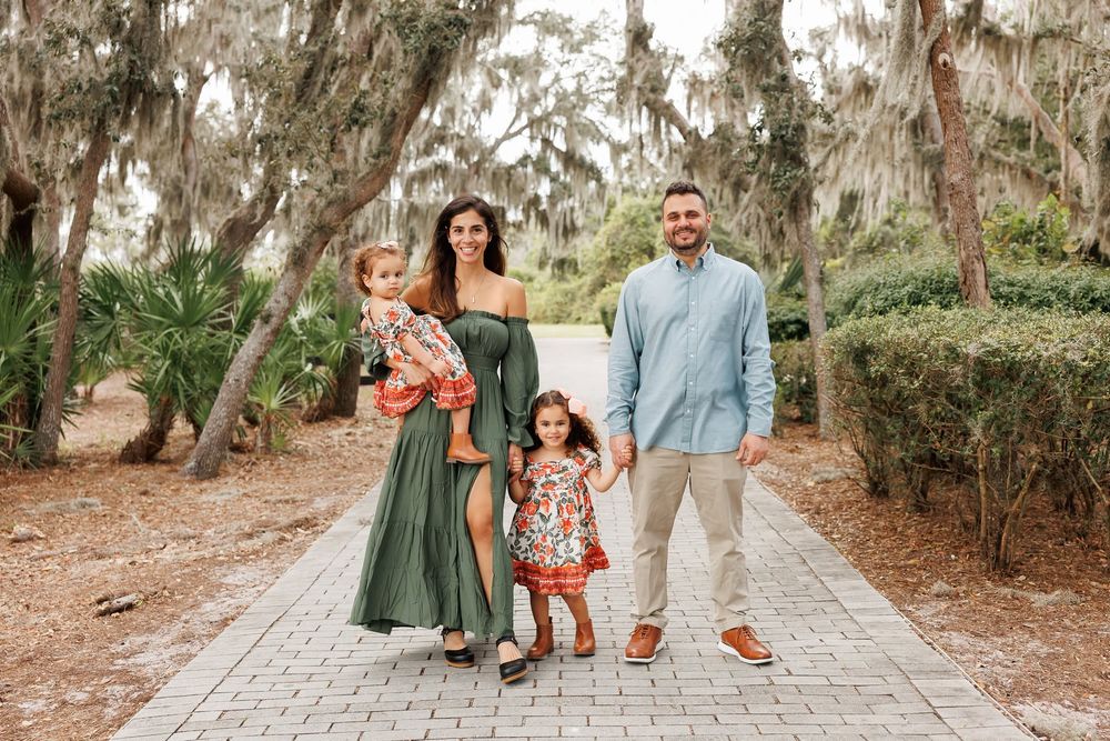 Family of four posing on a brick path surrounded by moss-draped trees, wearing coordinated green and floral outfits.