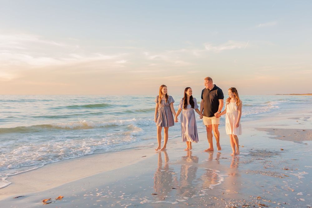 Family of four walking along a sandy beach at sunset with gentle ocean waves in the background.