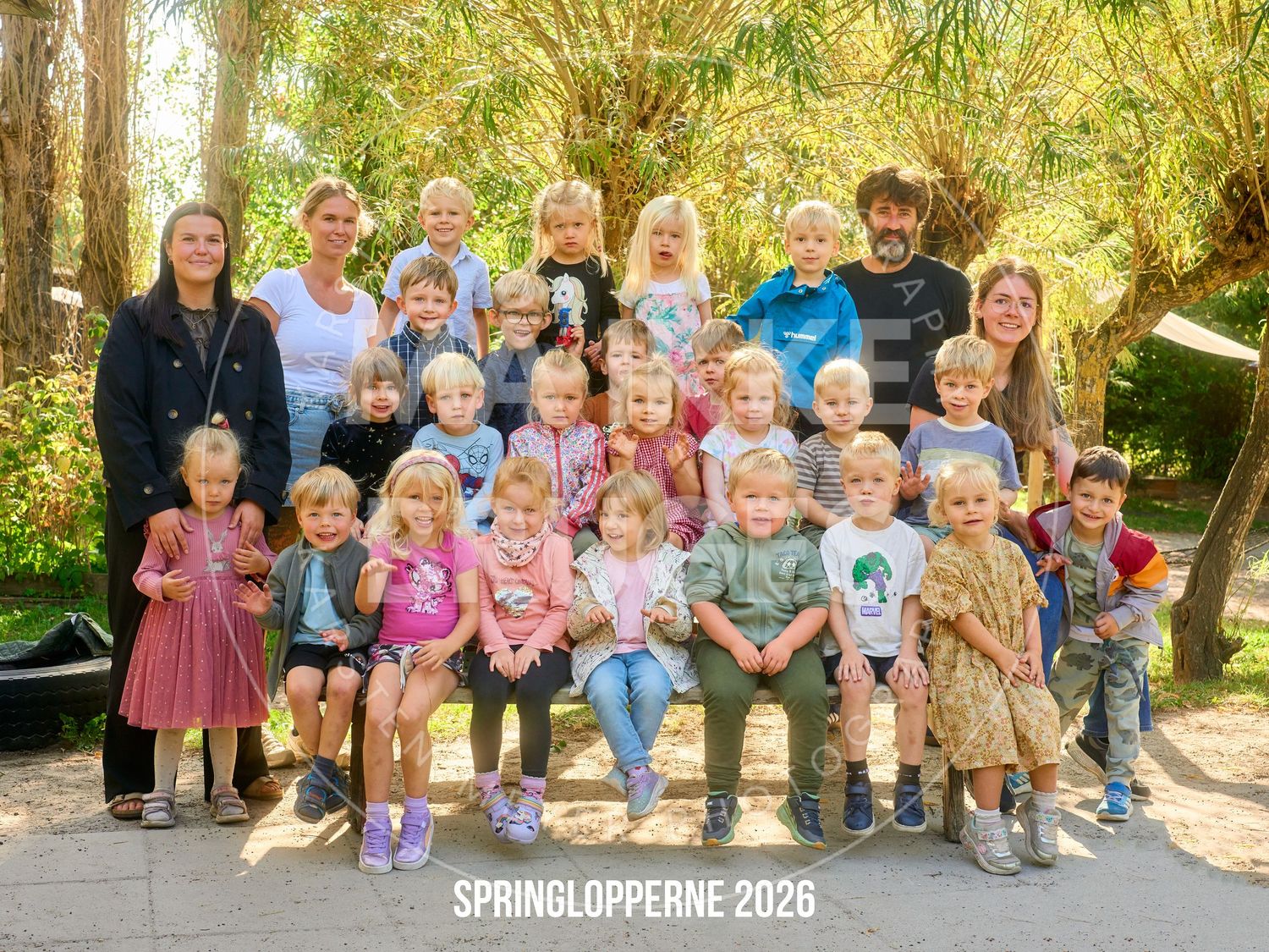 Group photo of children and teachers at Springlopperne 2026 daycare, posing outdoors among green trees.