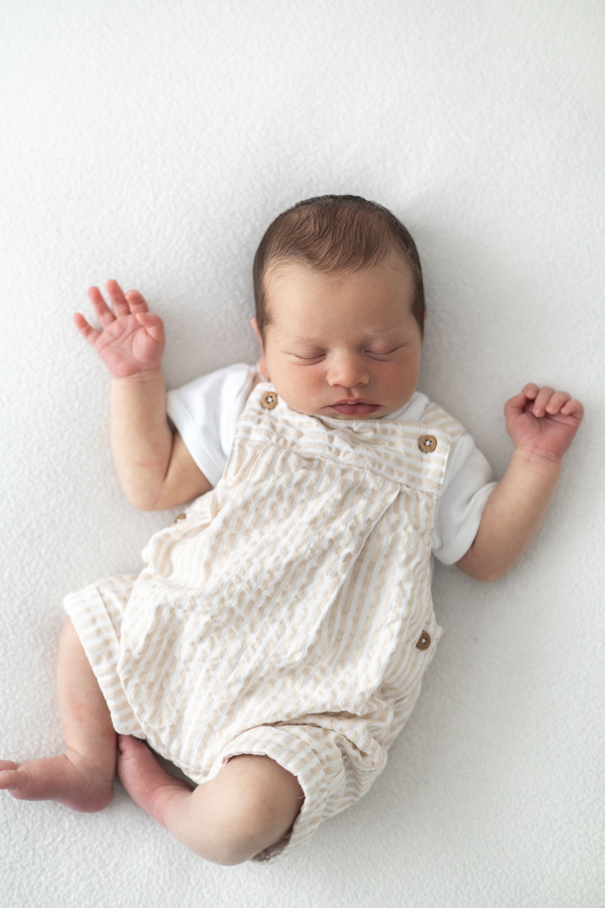 Sleeping newborn baby in beige patterned romper lying on white background with arms raised Newborn photographer Nottingham
