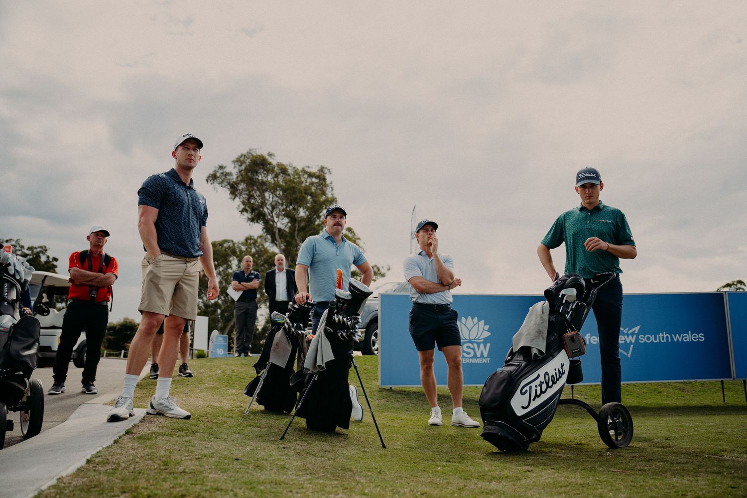 Golfers standing with Titleist golf bags on a green course under cloudy skies at a New South Wales golf event.