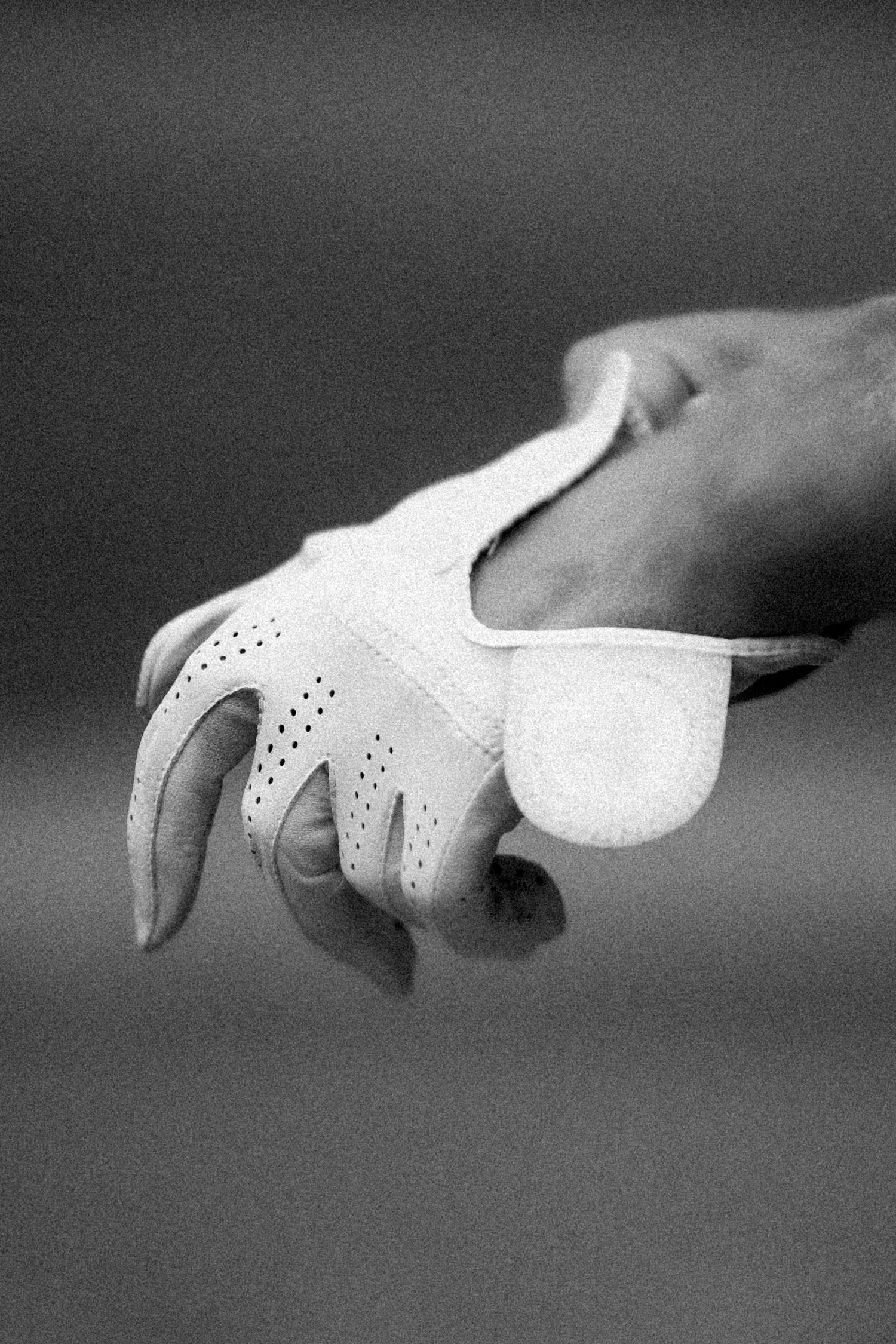 Close-up black and white photo of a hand wearing a white perforated leather golf glove.
