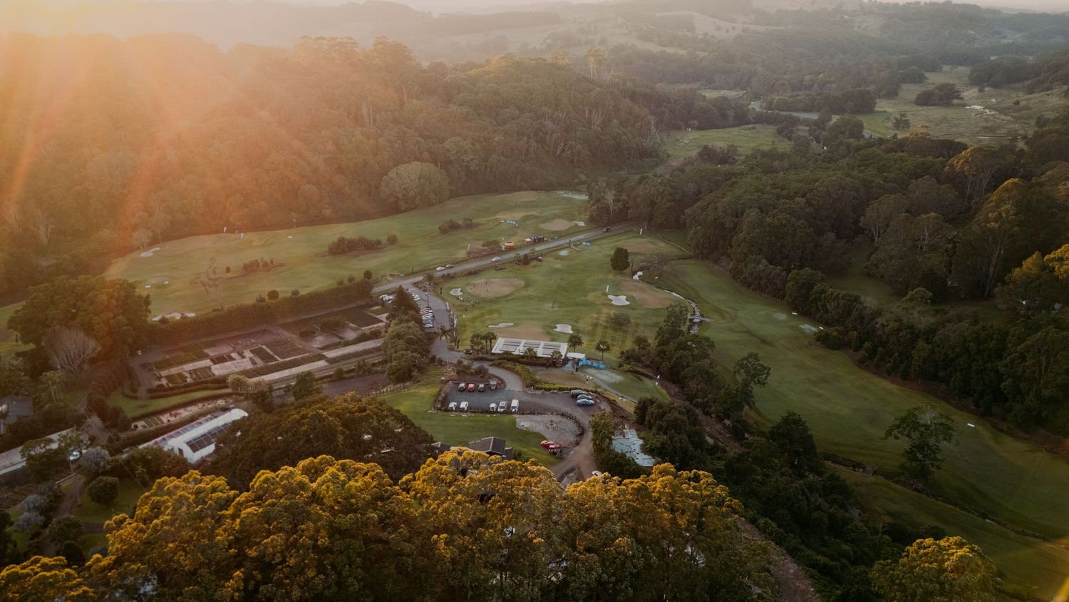 Aerial sunset view of a lush green golf course estate surrounded by dense forest and golden light.