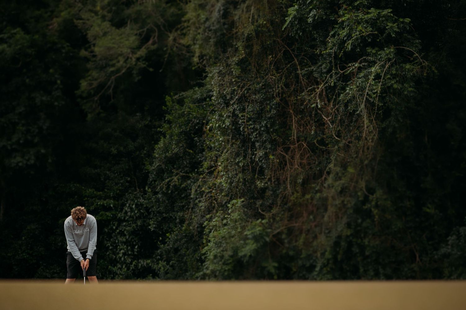 Golfer bent over putting on a lush green course surrounded by dense tropical forest trees.