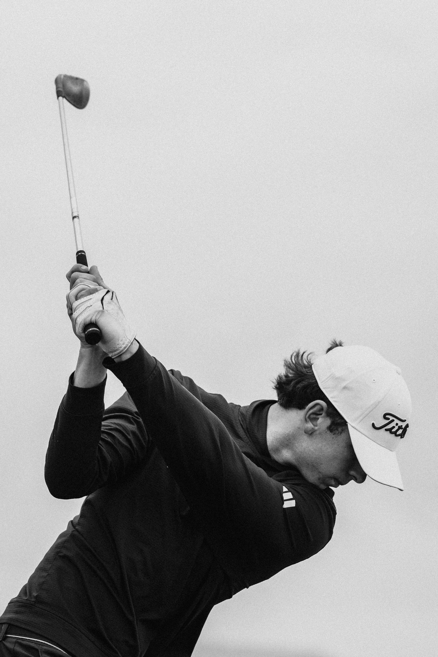 Black and white photo of a golfer in a Titleist cap completing a powerful golf swing with a driver.