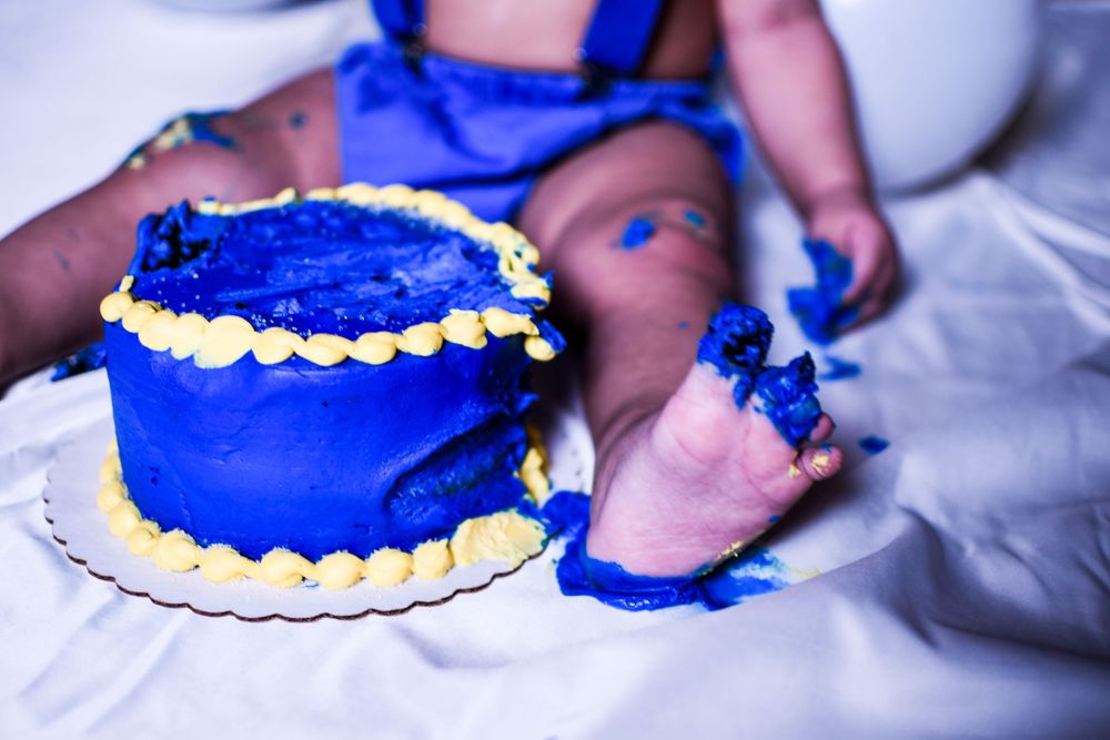 Baby's first birthday smash cake with blue frosting and yellow piping decorations on white background.