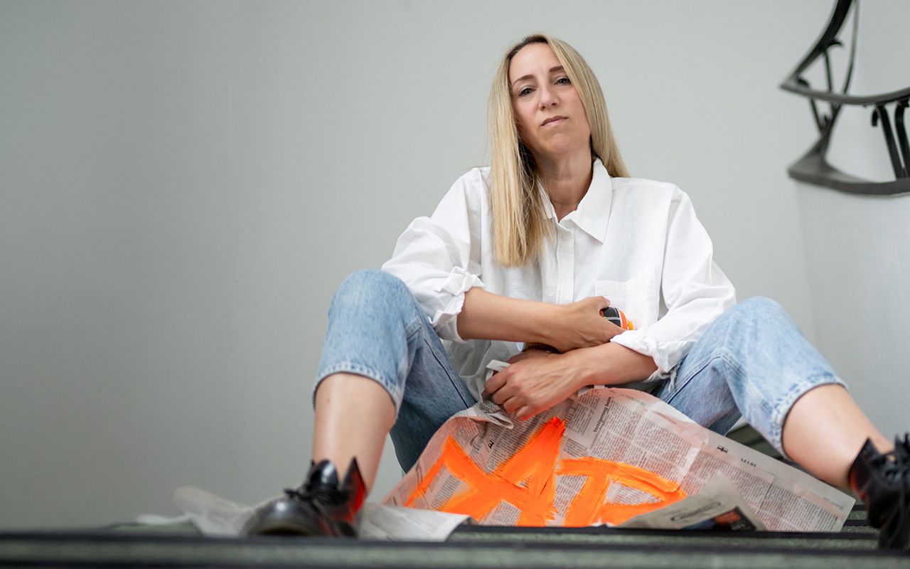 Künstlerin sitzt mit Zeitung und Spraydose auf einer weißen Treppe in der Kokerei Hassel in Gelsenkirchen.
