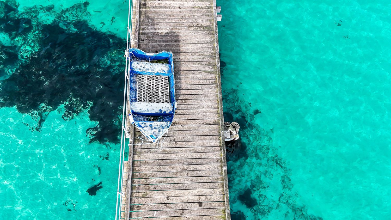 Aerial view of a small blue boat resting on a wooden dock surrounded by turquoise tropical water.