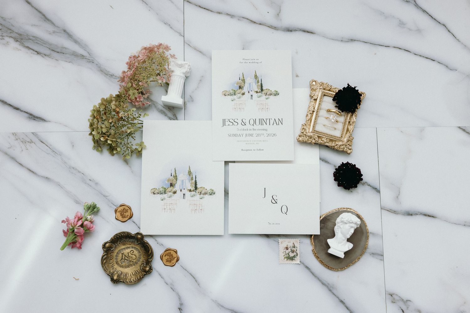 Elegant wedding invitation suite with watercolor details on marble surface, featuring floral accents and gold wax seals.
