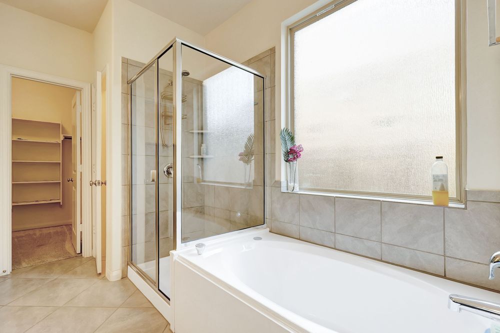 Bright bathroom featuring a walk-in glass shower, soaking tub, large window, and tile accents in neutral tones.