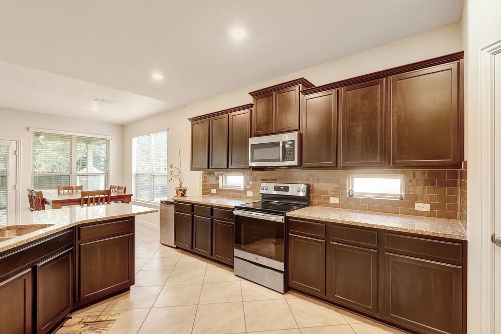 Modern kitchen with dark brown cabinets, stainless steel appliances, tile backsplash, and light tile flooring.