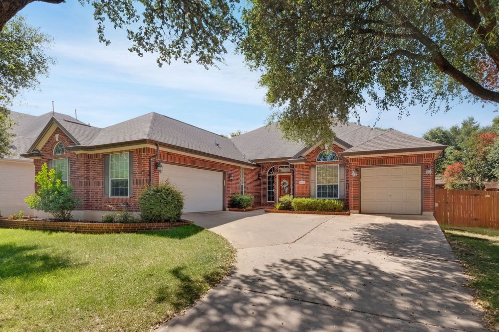 Brick ranch-style home with two-car garage, manicured lawn, and mature oak trees in a sunny suburban neighborhood.