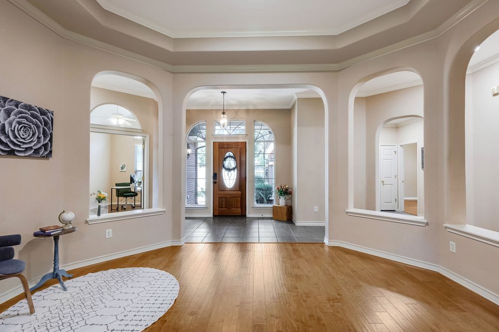 Elegant home entryway with arched doorways, hardwood floors, chandelier, and a grand wooden front door with natural light.