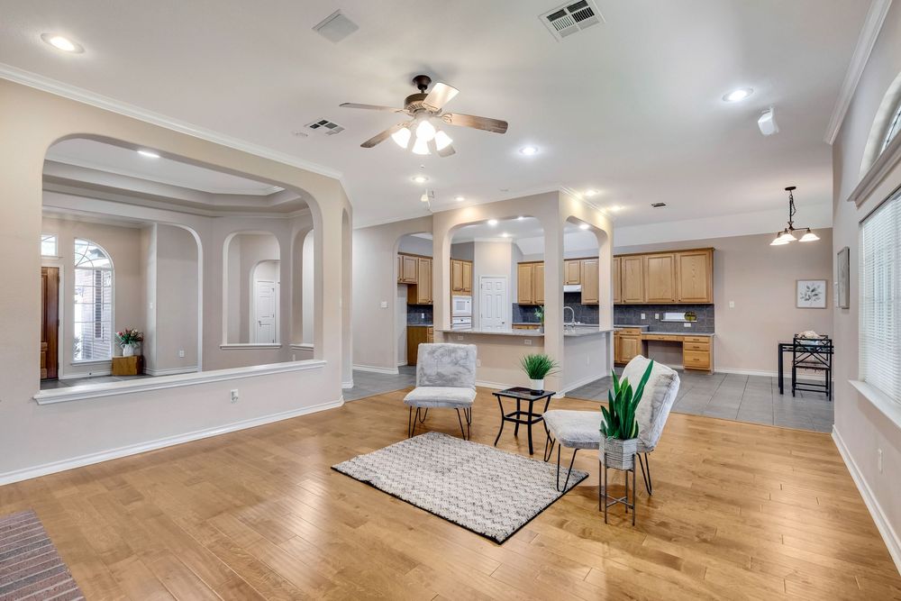 Spacious open-concept living room with hardwood floors, ceiling fan, arched doorways, and a modern kitchen visible in the background.