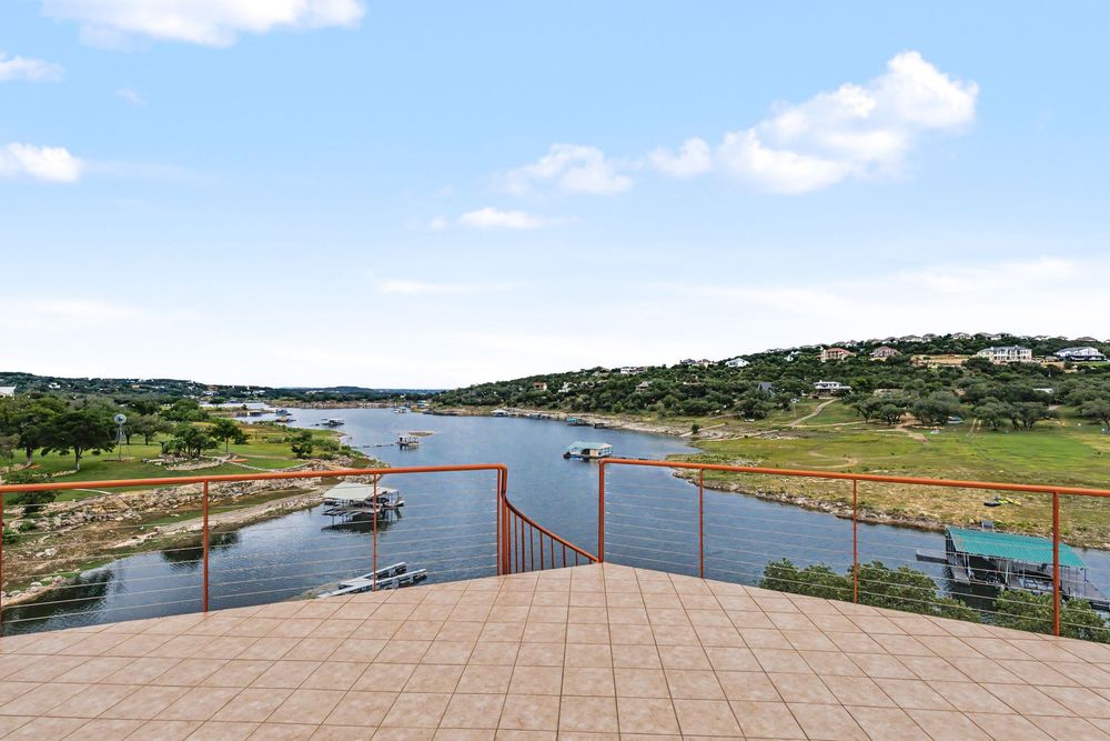 Stunning waterfront balcony view overlooking a serene lake with boats and lush green hills under a clear blue sky.