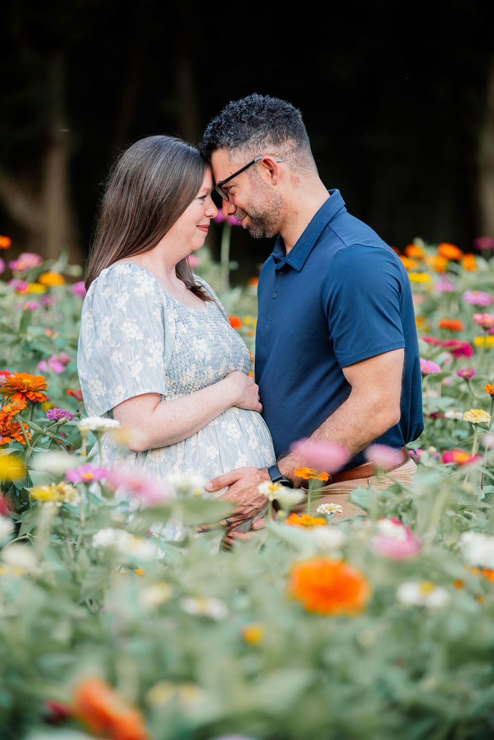 Pregnant couple embracing tenderly in a vibrant flower field, sharing an intimate moment surrounded by colorful blooms.
