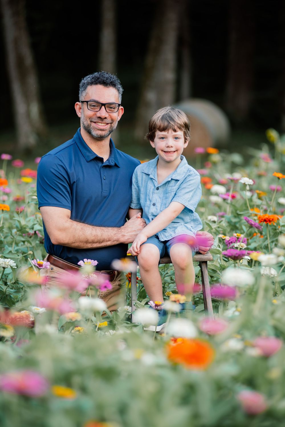 A father and young son smile together in a colorful zinnia flower field during a family portrait session.