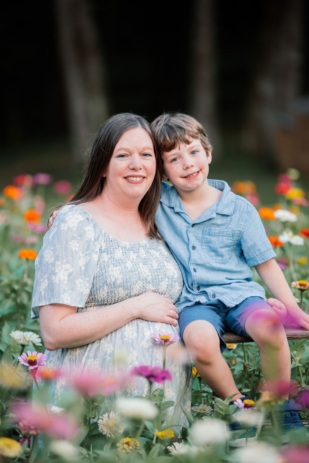Pregnant woman and young boy smiling together in a colorful flower garden during a maternity photo session.