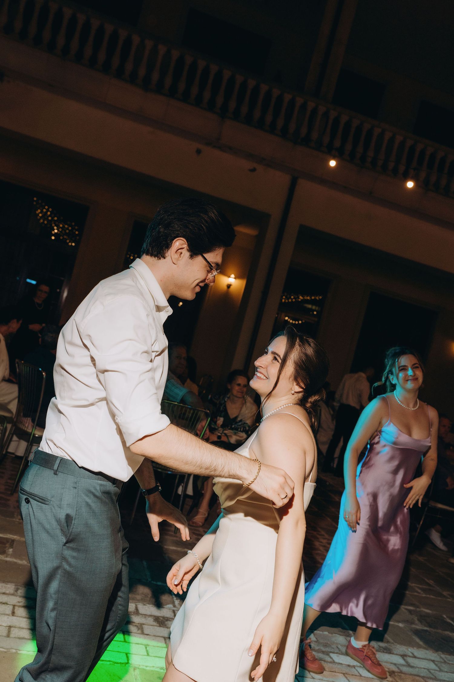 Couple dancing together at an outdoor wedding reception at night with colorful lights.