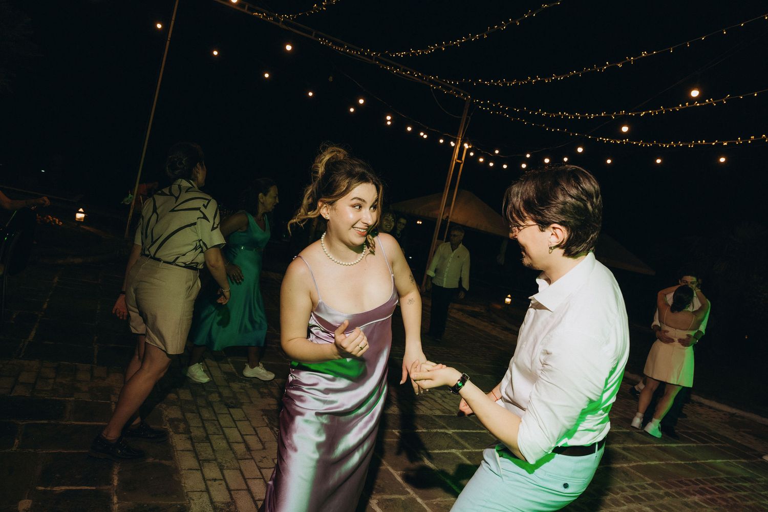 Two people dancing together at an outdoor evening event with string lights overhead.