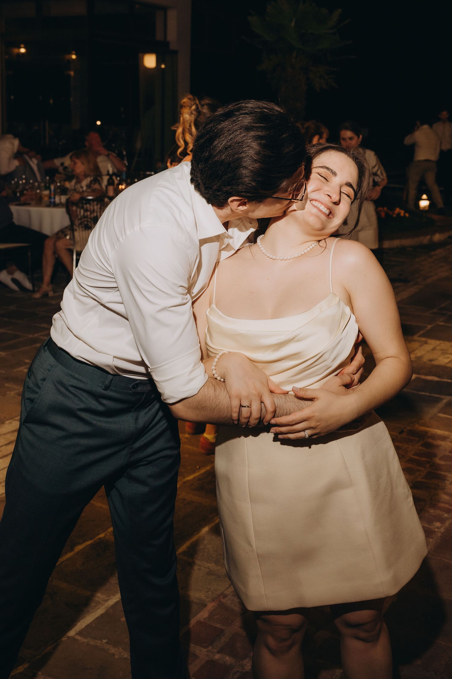Couple sharing a romantic dance embrace at a wedding reception, woman in cream mini dress smiling with eyes closed.
