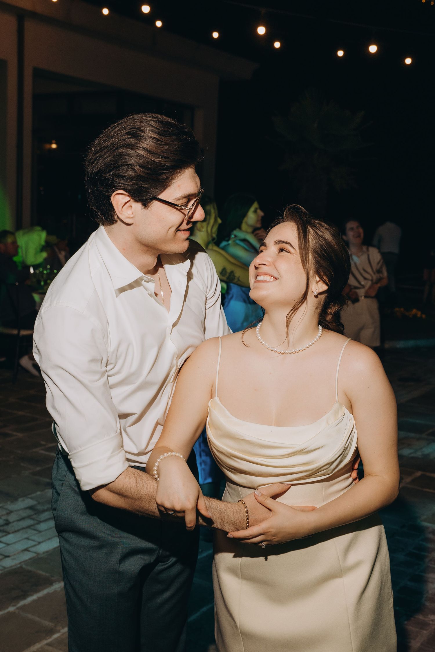 Couple sharing a romantic dance at an outdoor evening wedding reception under string lights.