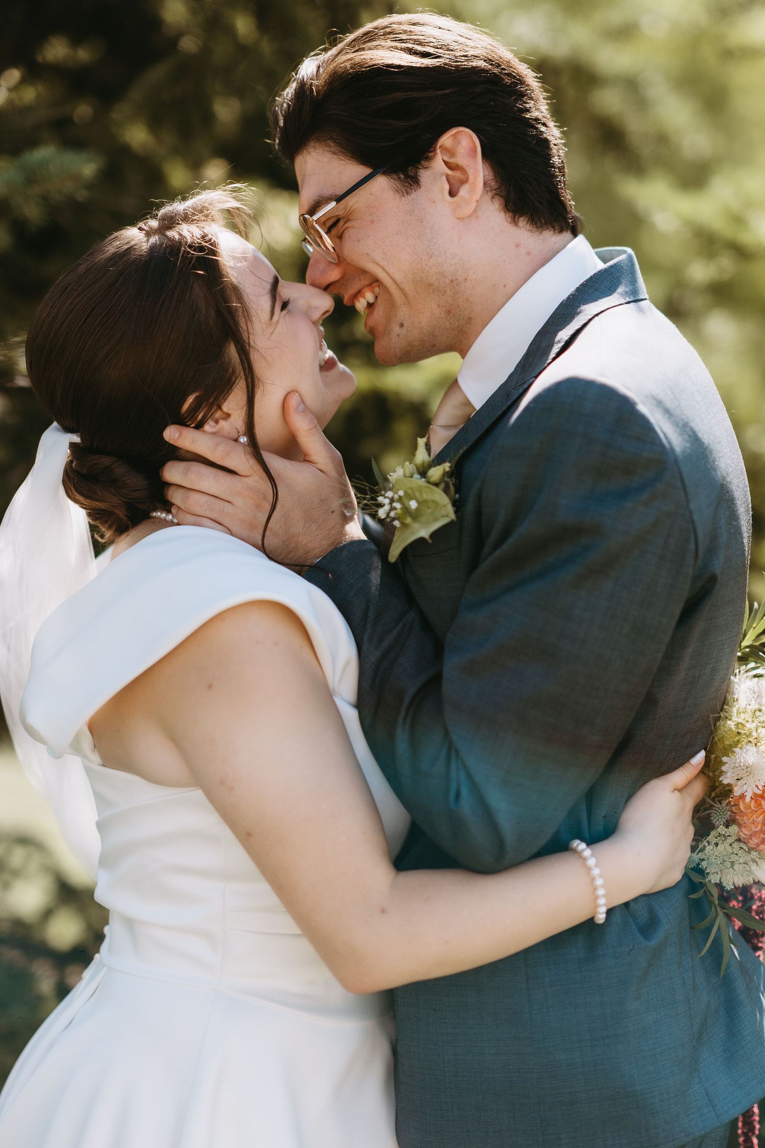 A joyful bride and groom share a romantic moment, nearly kissing, dressed in wedding attire outdoors.