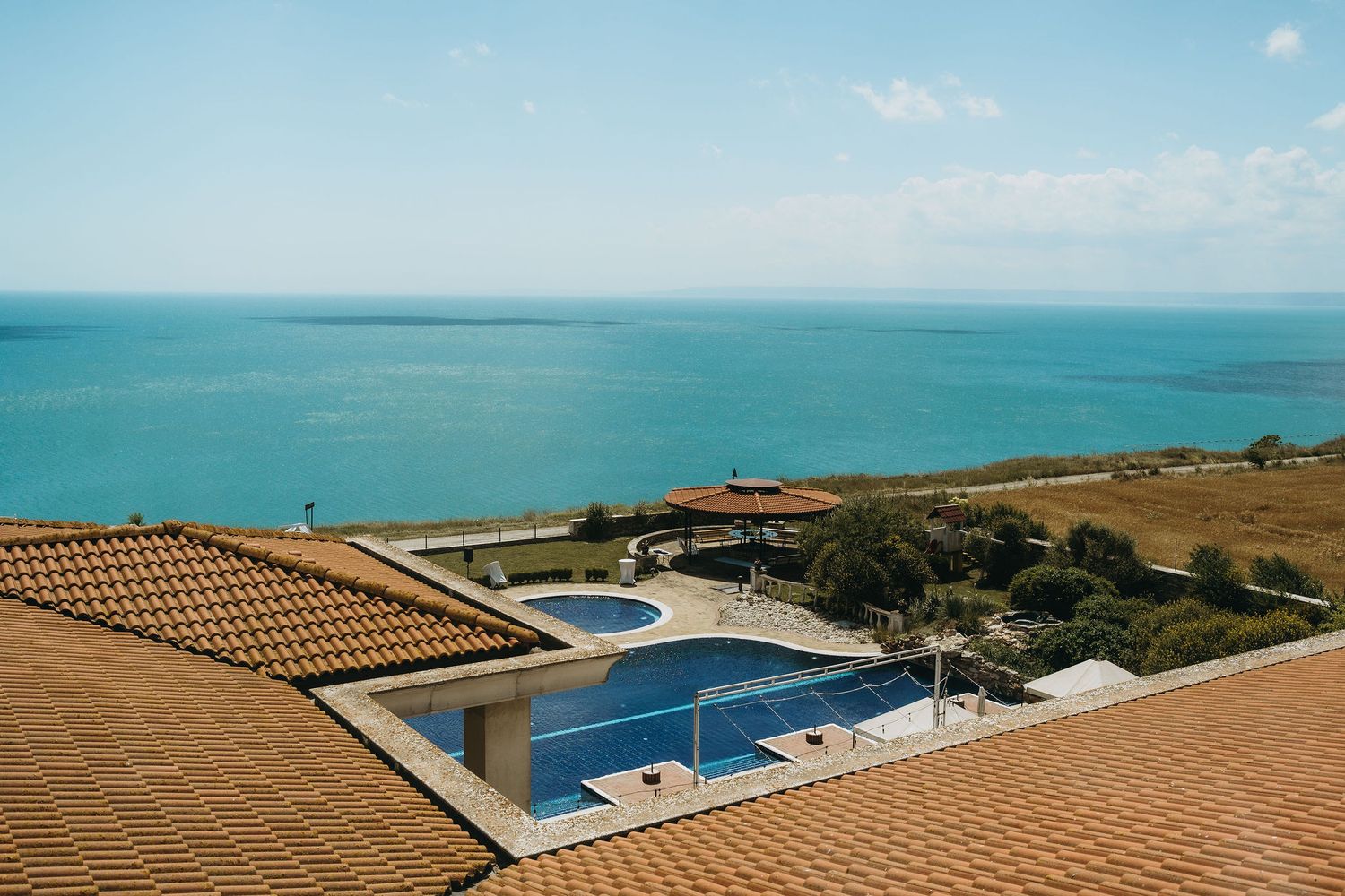Aerial view of luxury villa with two pools overlooking turquoise sea under clear blue sky.