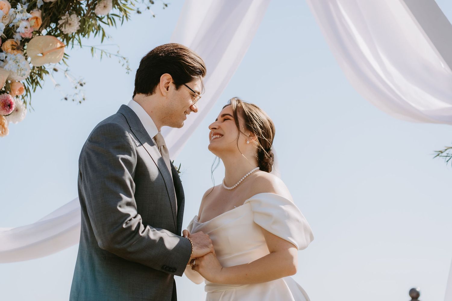 A couple shares a joyful moment at an outdoor wedding ceremony, bride in white gown and groom in gray suit.