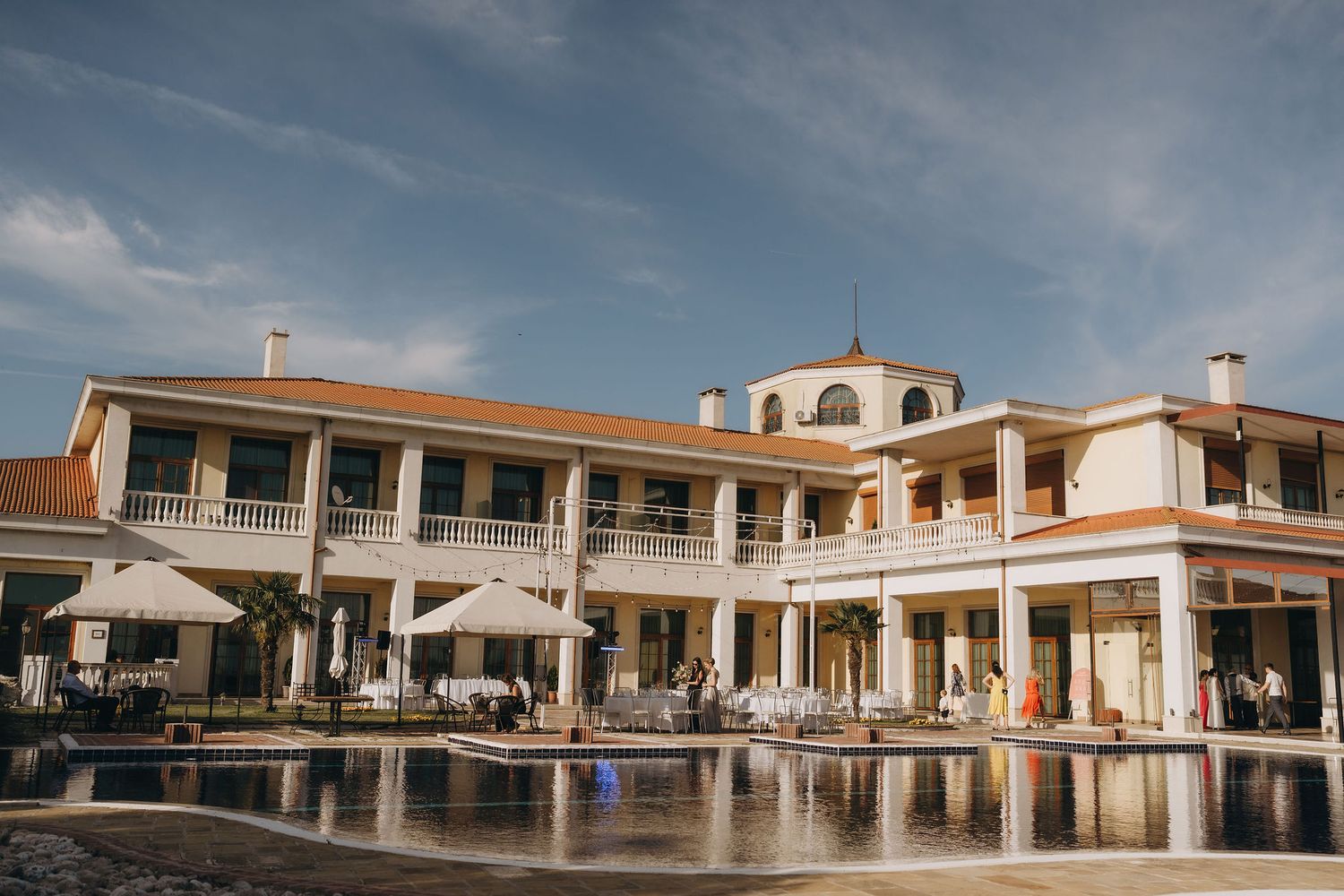 Elegant resort villa with outdoor pool, white umbrellas, and tropical landscaping under a blue sky.