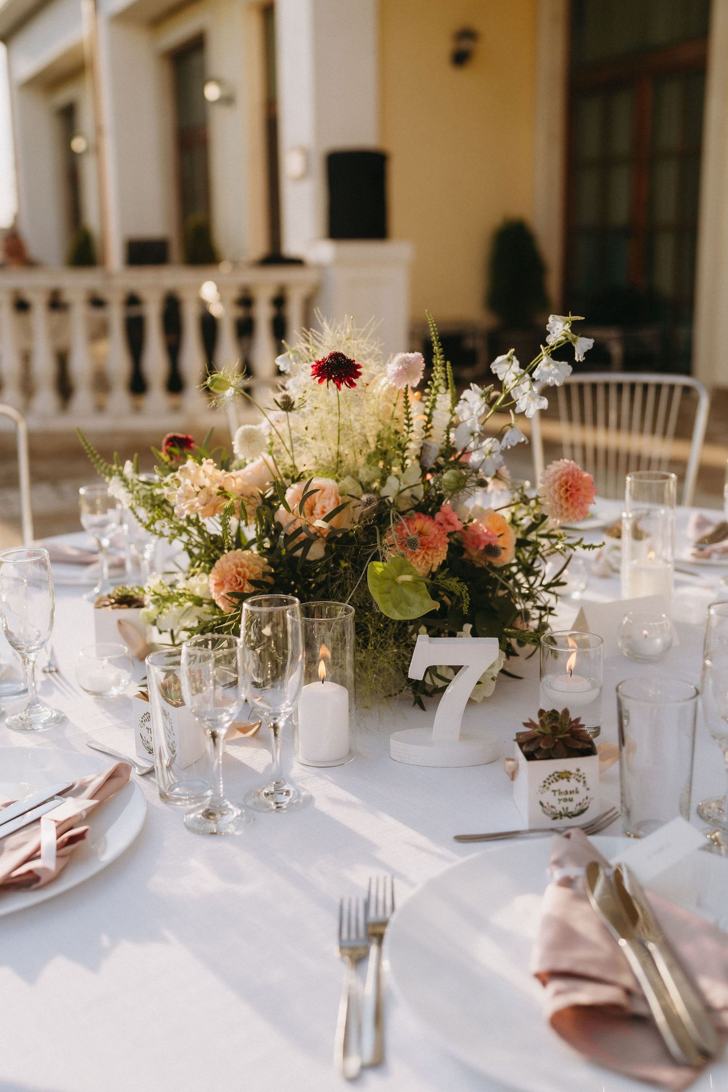 Elegant wedding table setting with floral centerpiece, candles, champagne flutes, and pink napkins at outdoor reception.