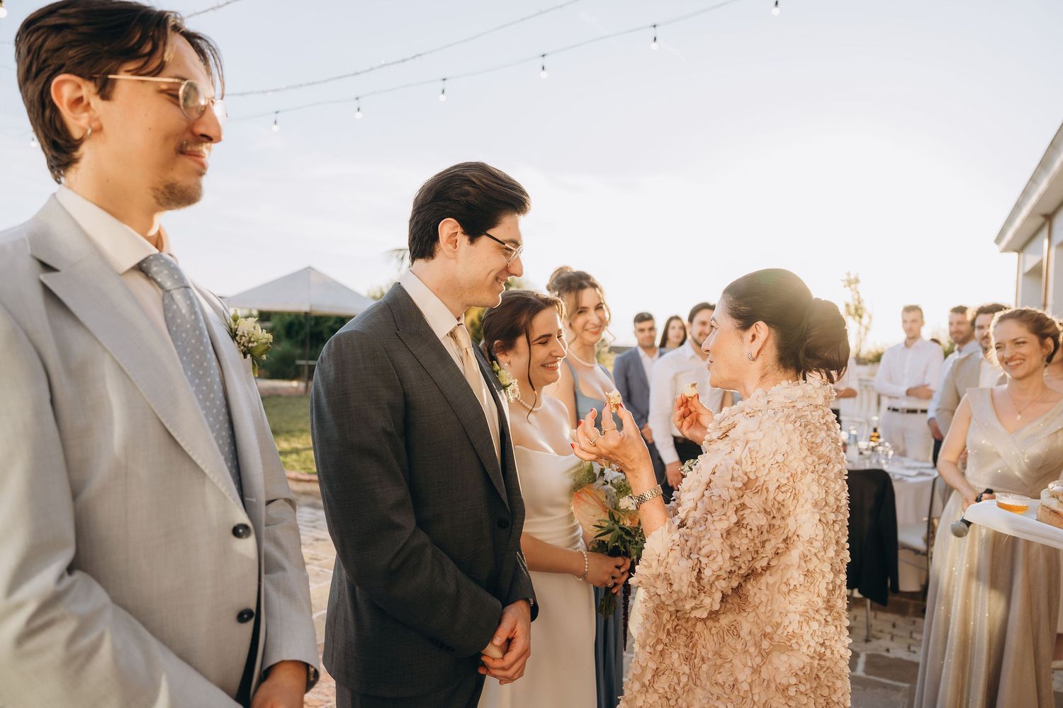 Elegant outdoor wedding reception with guests congratulating the newlyweds, string lights and tent in background.