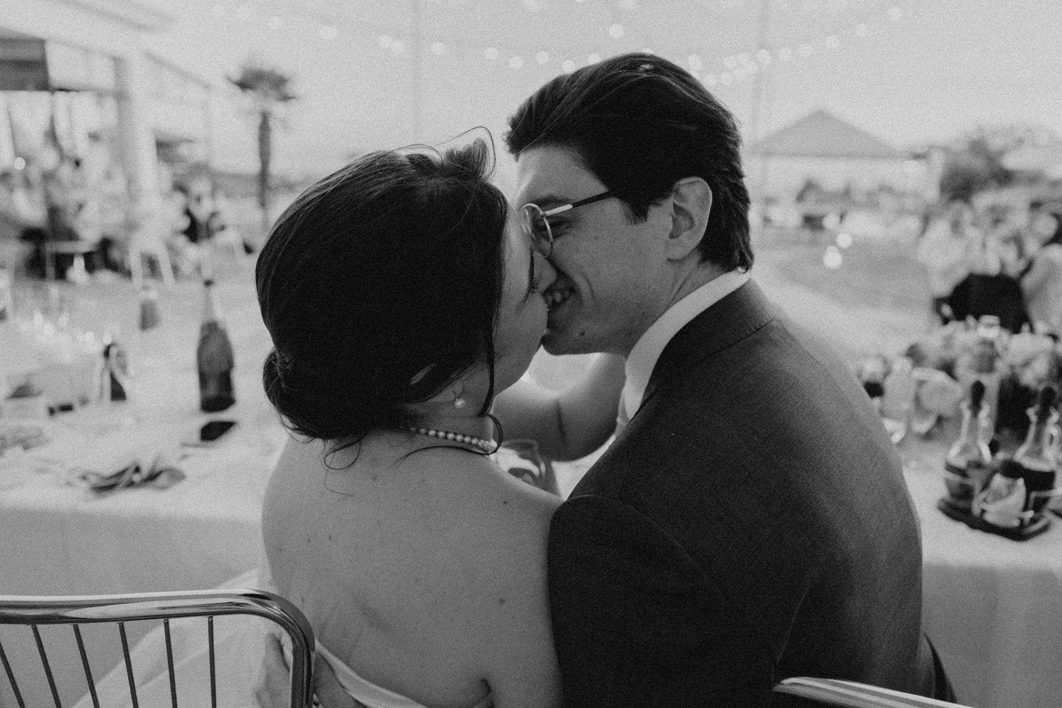 Black and white photo of a bride and groom sharing a kiss at their wedding reception.