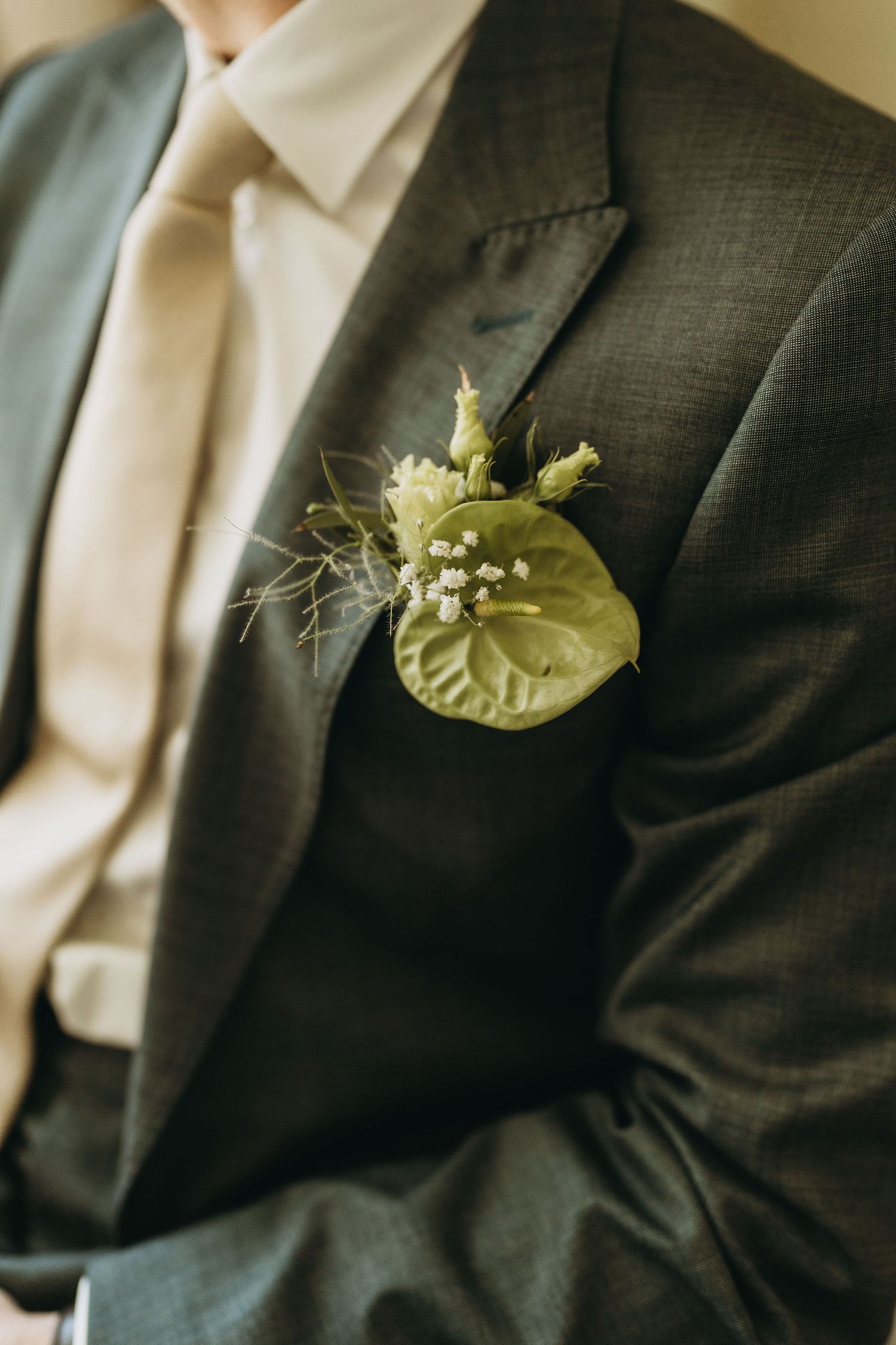 Close-up of a groom wearing a dark suit with a green anthurium boutonniere and baby's breath on his lapel.